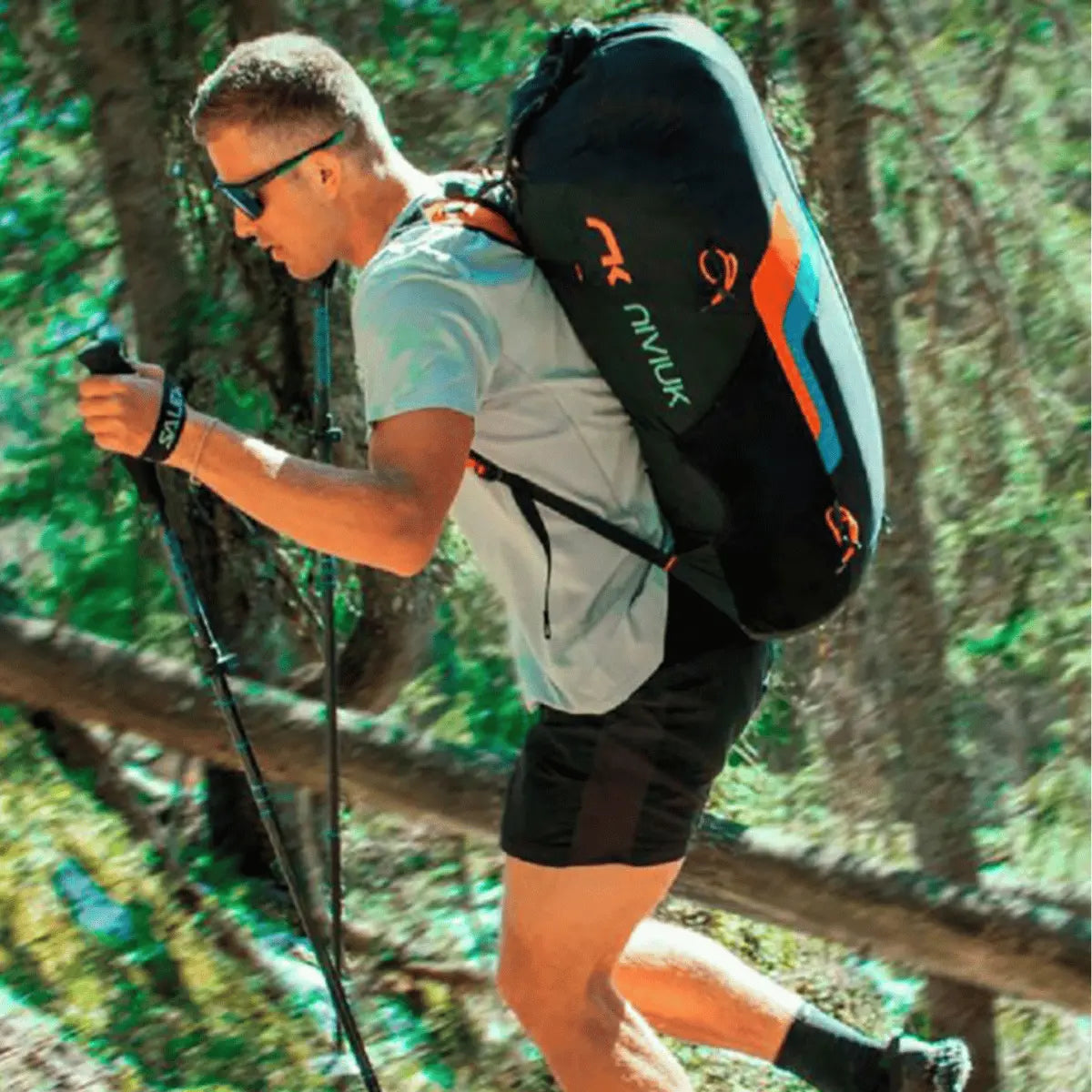 Ein Mann mit einem Niviuk Expe Race Hike & Fly Rucksack wandert mit Trekkingstöcken durch einen Wald.