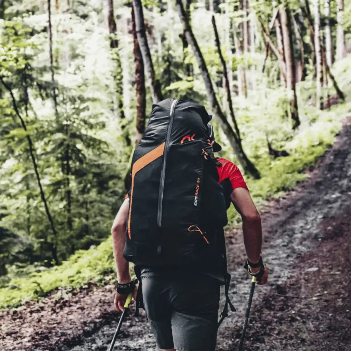 Mann mit großem schwarzem Niviuk Expe Race Hike & Fly Rucksack und orangefarbenen Akzenten wandert auf einem Waldweg.