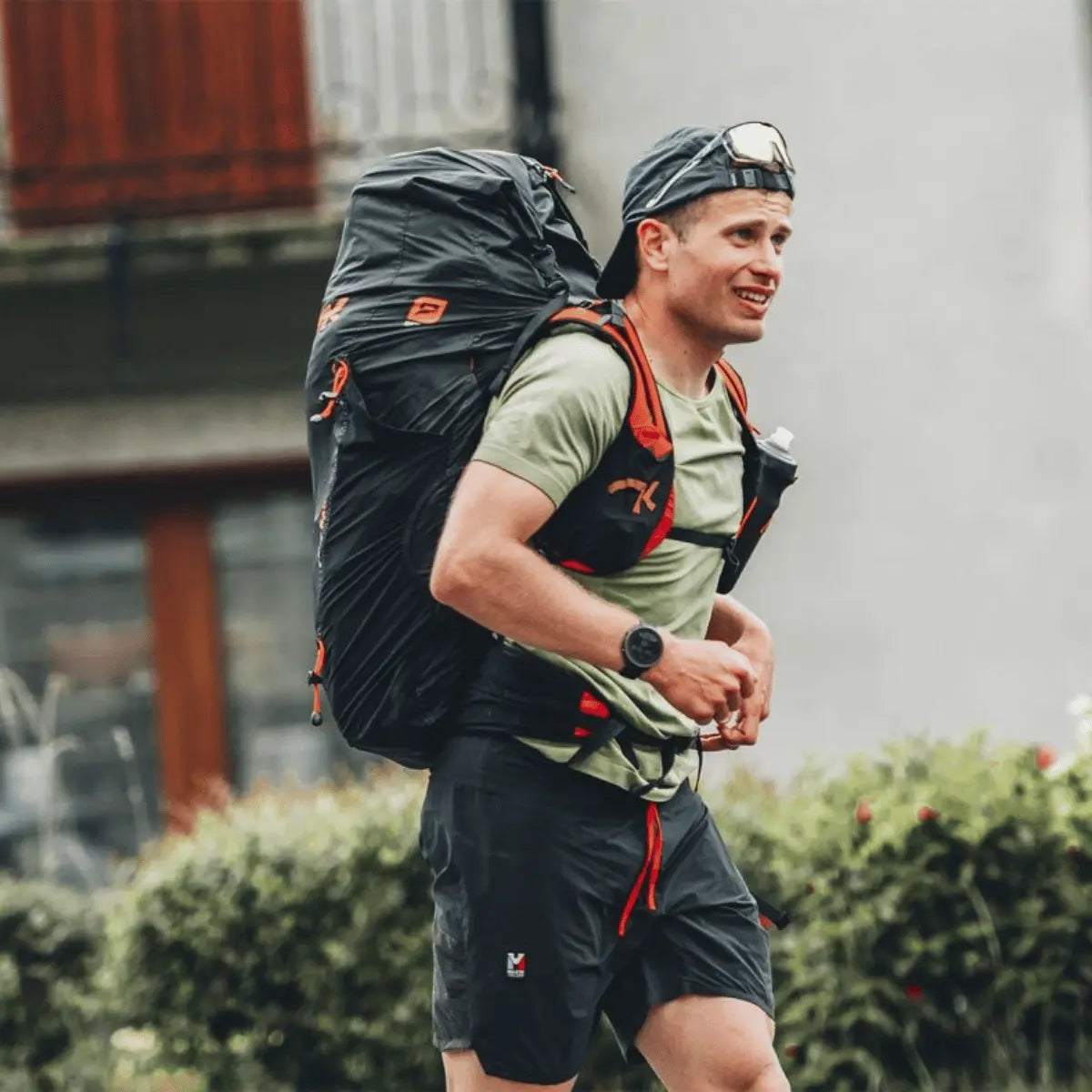 Ein Mann mit einem großen schwarzen Niviuk Expe Race Hike & Fly Rucksack und einer Laufweste, der einen Bergauflauf absolviert. Der Rucksack hat rote Akzente und eine Trinkflasche ist sichtbar.