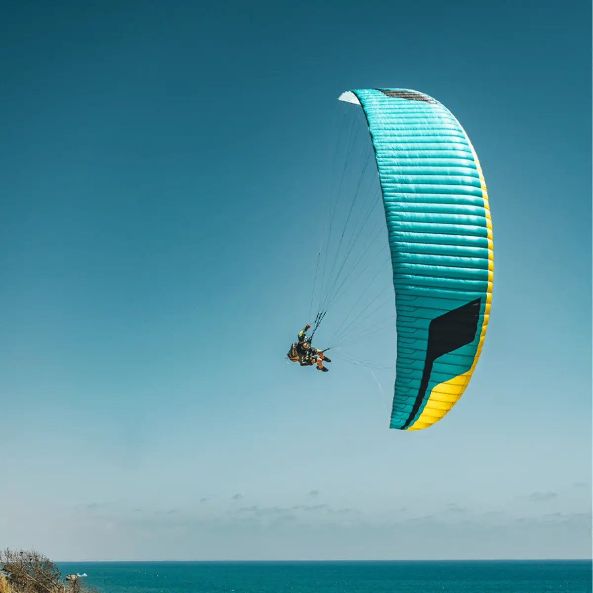 Ein Niviuk Jester Parakite mit blau-gelbem Schirm fliegt über dem Meer.