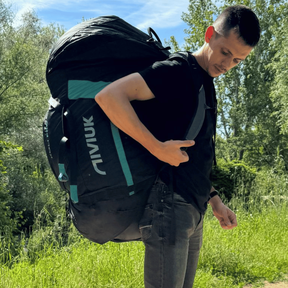 Niviuk Koli Pro Tandem Schnellpacksack getragen von einem tandempiloten mit Natur im Hintergrund. Ideal für schnelles, sicheres Packen von Flugausrüstung, mit elastischem Kordelzug und verstellbaren Trageriemen.