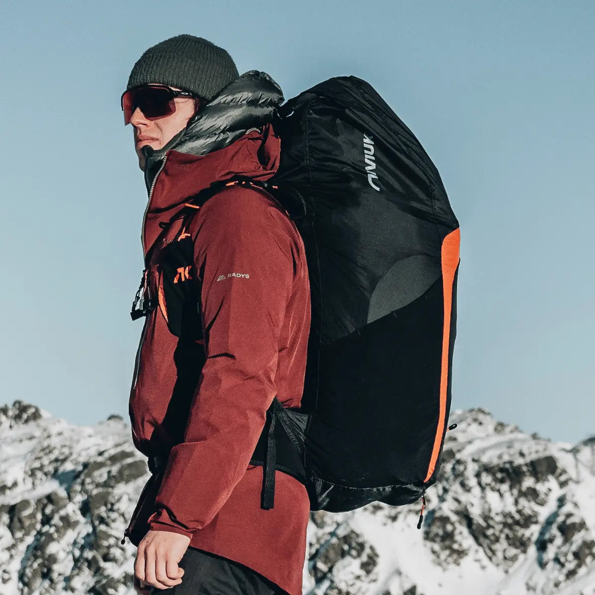 Mann mit Niviuk Kooper P Gleitschirm-Gurtzeug im Winter, schwarzer Rucksack mit orangefarbenen Akzenten und Niviuk-Logo.