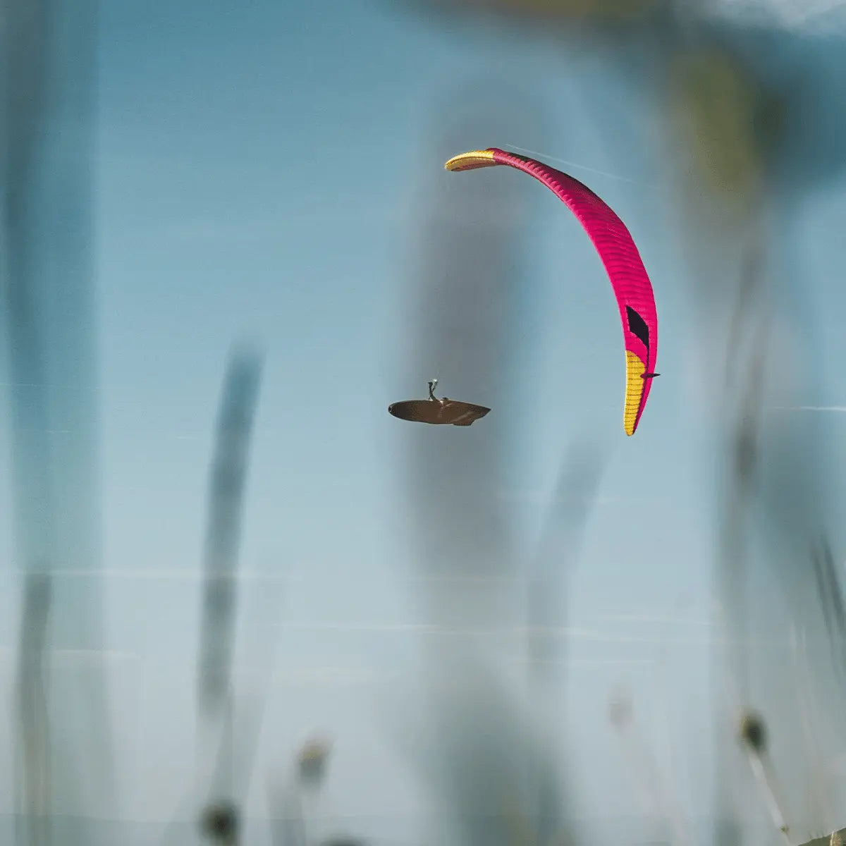 Ein Hochleistungs-Gleitschirm Niviuk Peak 7 (EN-D) in leuchtendem Pink und Gelb fliegt hoch am blauen Himmel, während ein Pilot darunter schwebt.