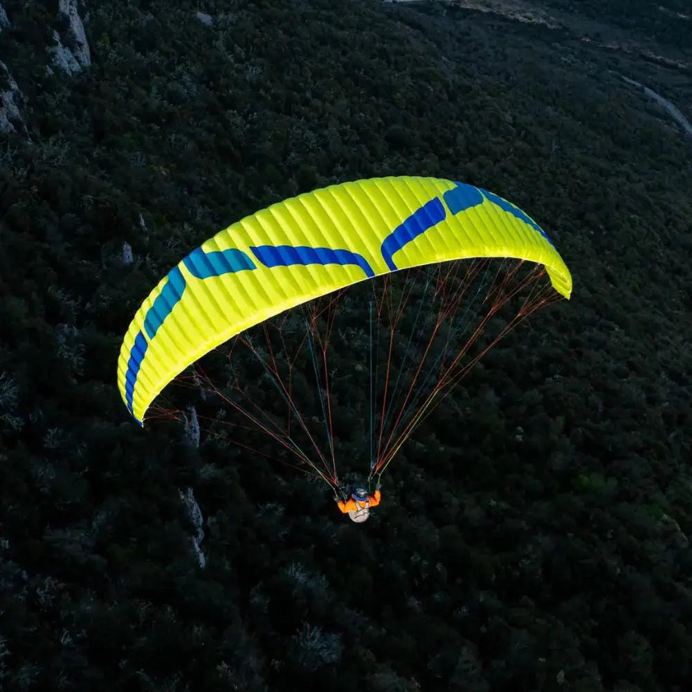 Person beim Paragliding mit Ozone Buzz Z7 Schirm in der Luft, bekannt für hohe Sicherheit und Agilität, geeignet für XC-Flüge.