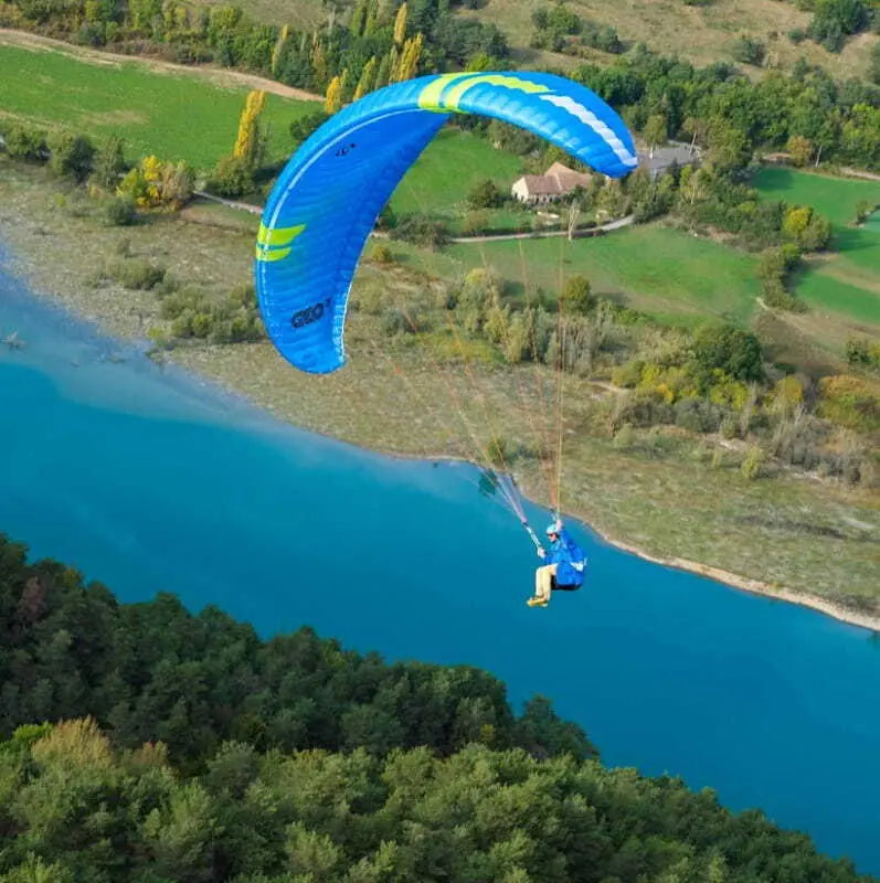 Person paraglidet mit Ozone Geo 7 über Fluss, zeigt Leistung und Agilität, ideal für XC-Flüge und Hike & Fly.