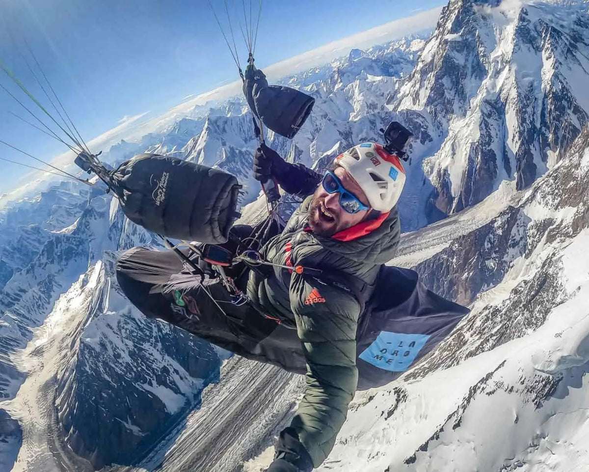 Mann beim Paragliding über verschneiten Bergen, trägt WindsRiders Warm Sleeve Muffles K2-ZIP, ideal für kalte Flüge mit echter Daunenisolierung.