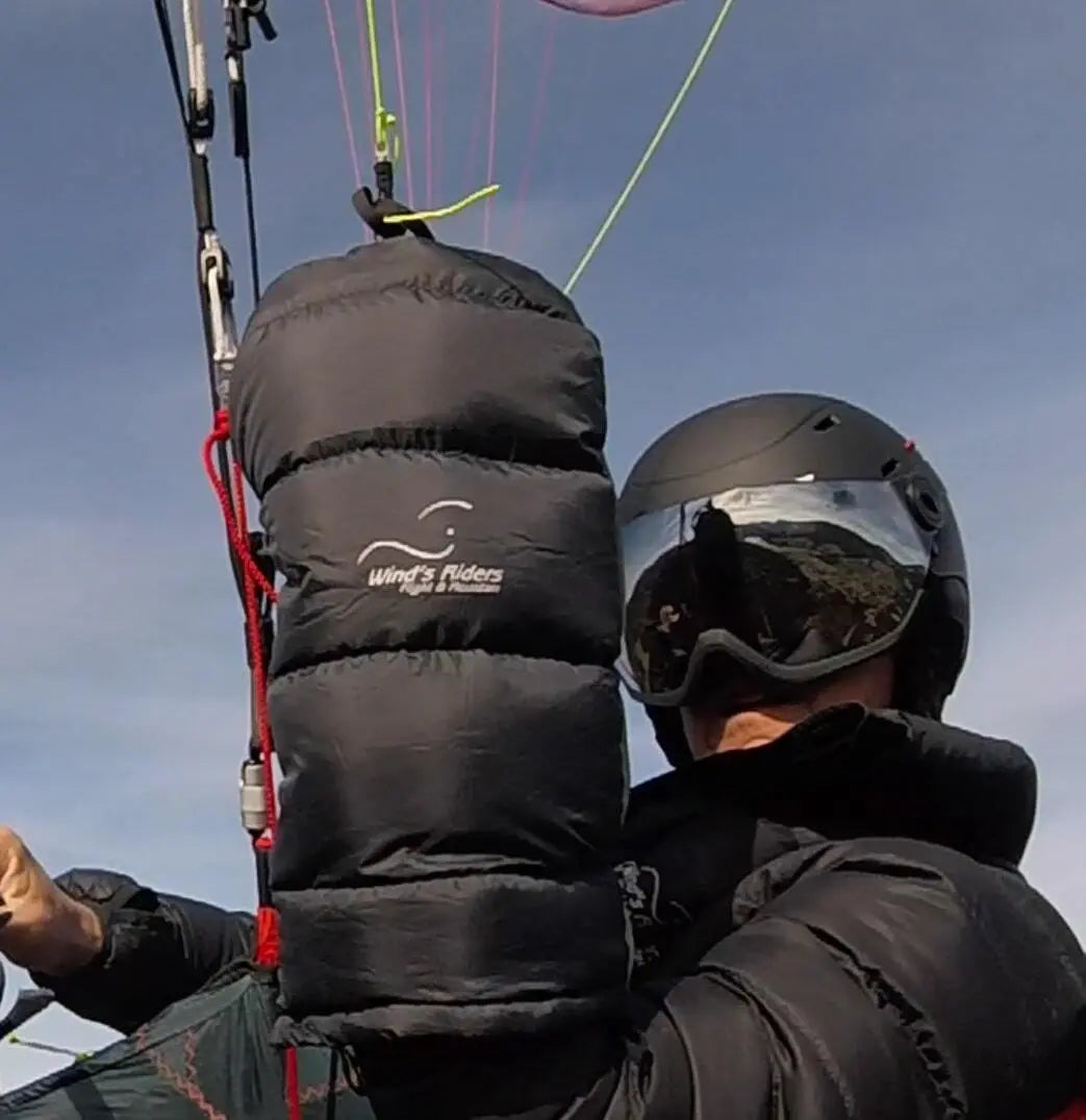 Person mit Helm hält WindsRiders Warm Sleeve Muffles - Everest, speziell entwickelt für extreme Kälte und Paragliding über hohen Bergketten.