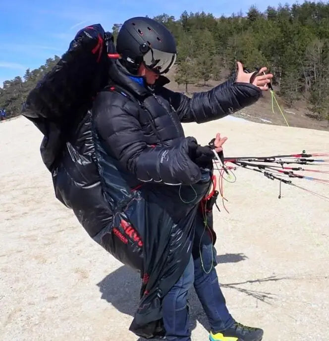 Mann mit Helm und Gleitschirmanzug, nutzt WindsRiders Warm Sleeve Muffles - Everest, ideal für extreme Winterflüge, schützt Hände bis -30°C.
