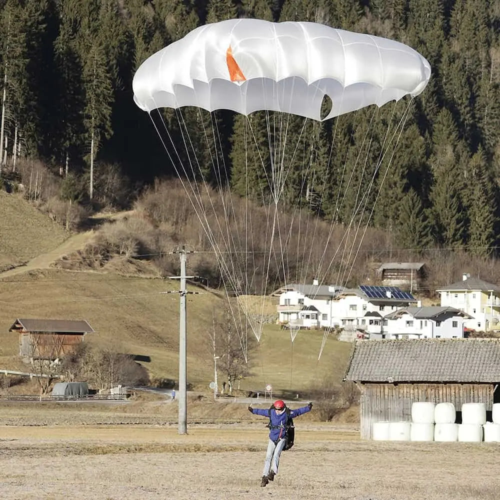 Person mit Charly TargetCross Basic Light Notschirm während des Einsatzes, mit erkennbarer weißer Kappe und orangefarbener Spitze, ideal für sicheres Paragleiten.