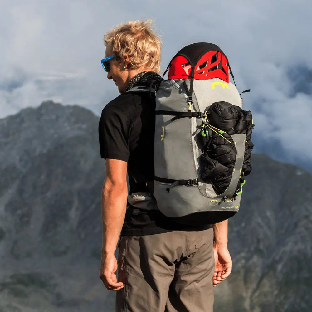 Mann mit Niviuk Roamer 2 Hike&Fly Gurtzeug und Schlafsack, bereit für Bergabenteuer, zeigt Komfort und Effizienz des innovativen Tragesystems.