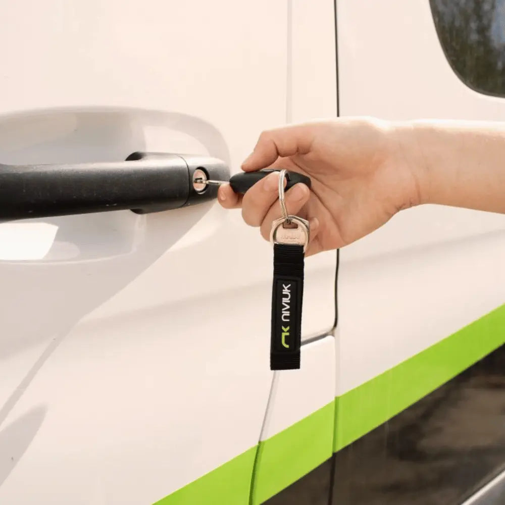 Hand mit Niviuk Schlüsselanhänger steckt Autoschlüssel in Türschloss eines weißen Fahrzeugs. Der Schlüsselanhänger symbolisiert Paragliding-Leidenschaft.