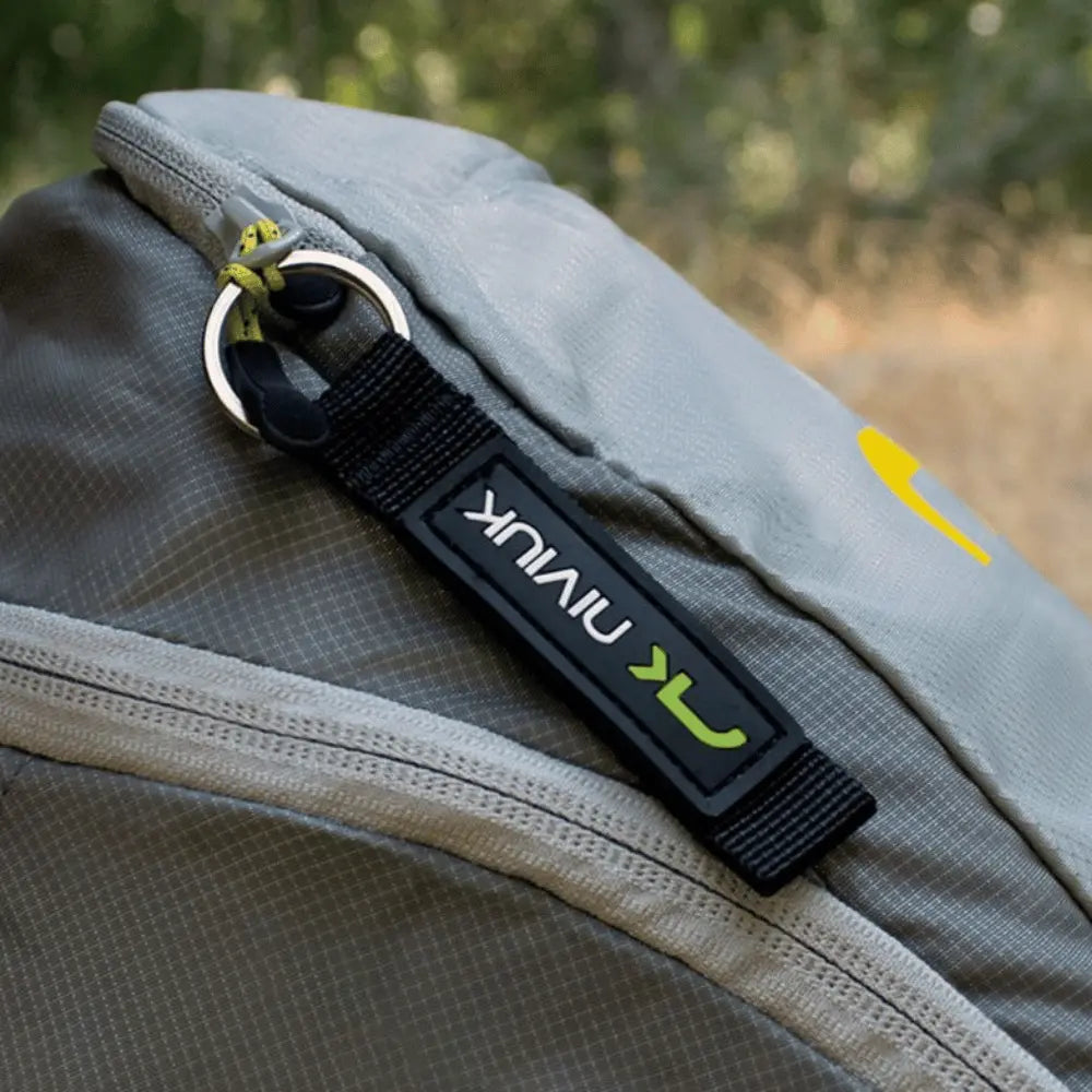 Niviuk Schlüsselanhänger am grauen Nylonrucksack befestigt, ideal für Paragliding-Fans; robustes Design mit grün-weißem Logo, perfekt für Flugtaschen oder Schlüsselbund.