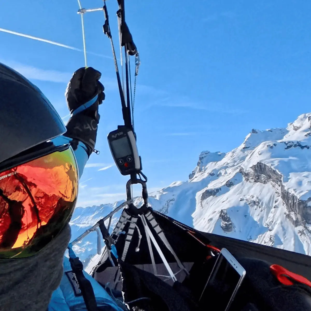 Syride Alti V4 Ultraleichtes Alti Vario mit integriertem GPS und variometrischer Anzeige, befestigt an einem Gleitschirm-Helm mit Skibrille.