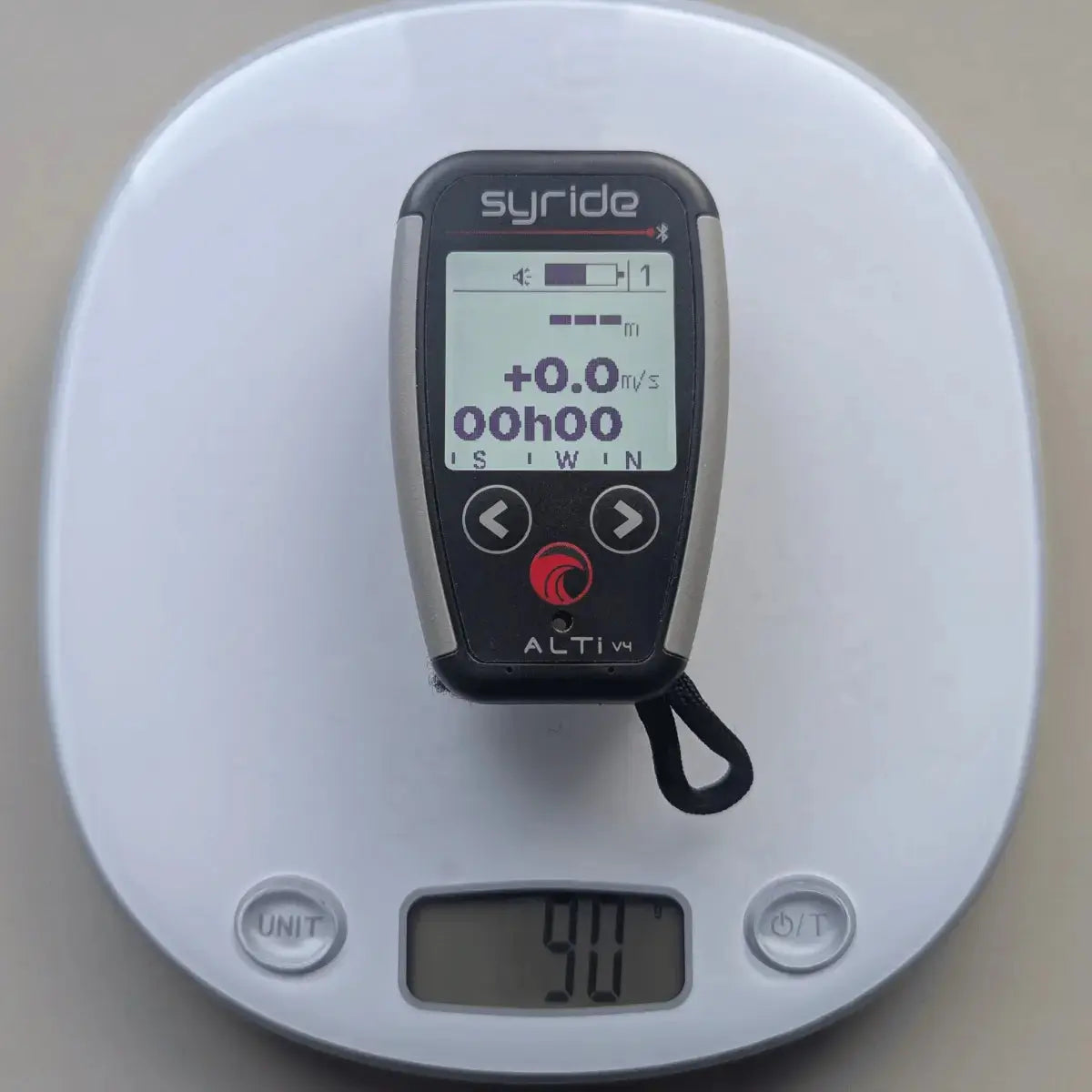 Syride Alti V4 Vario mit Display, Tasten und Lanyard auf einer digitalen Küchenwaage, die 90g anzeigt.