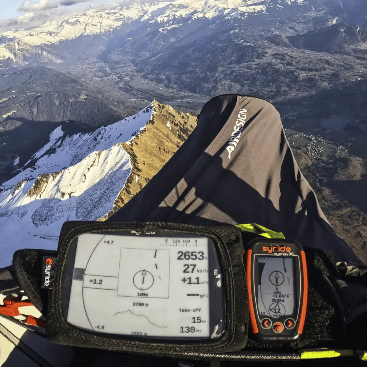 Syride Evo V2 Variometer in Nahaufnahme während eines Gleitschirmflugs über schneebedeckte Berggipfel, zeigt wichtige Flugdaten und Navigation für Paragliding24.ch.