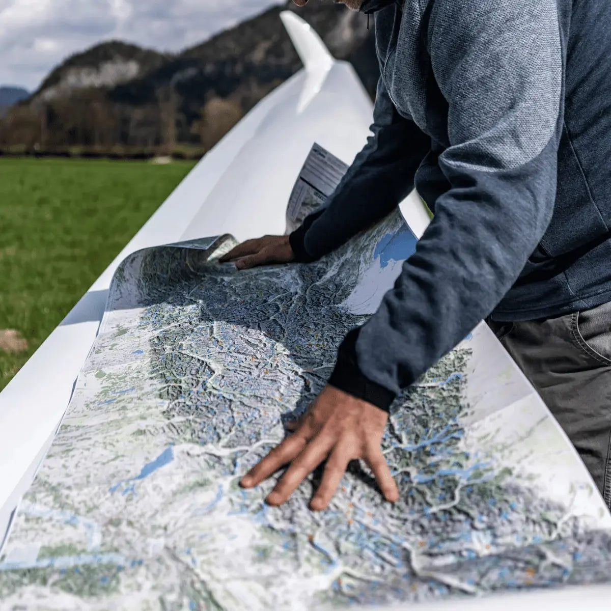 Mann mit Thermik- und Föhnkarte Alpenraum auf einem Segelflugzeugflügel, detaillierte topografische Darstellung.