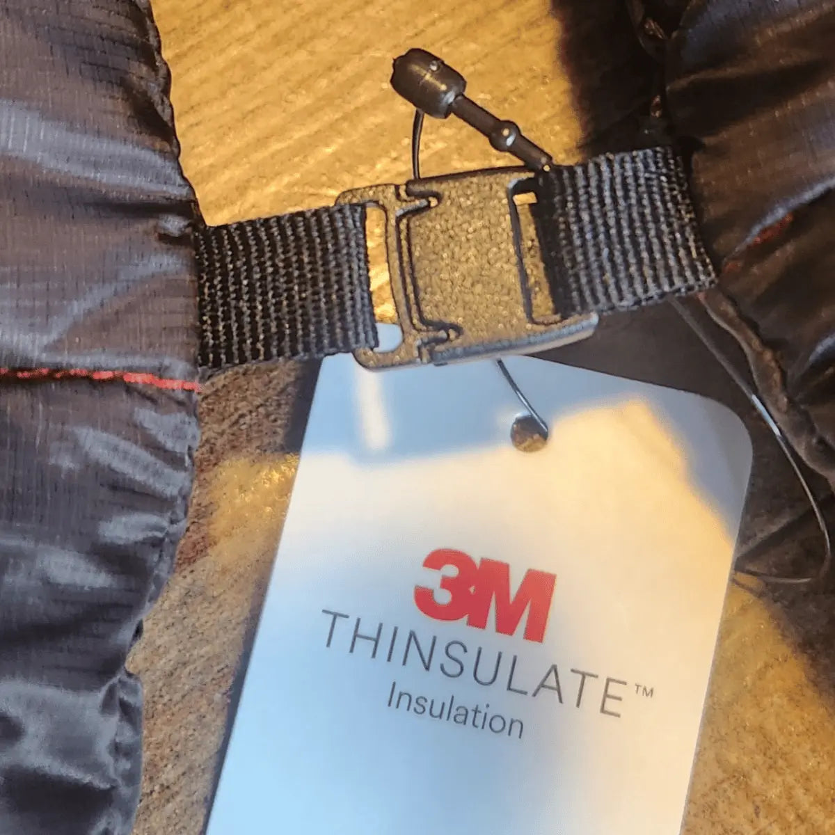 Detailaufnahme eines schwarzen Windsriders K2 Magnet Muffles mit 3M Thinsulate-Isolierung, gezeigt mit einem schwarzen Gurtbandverschluss und einem Anhänger.