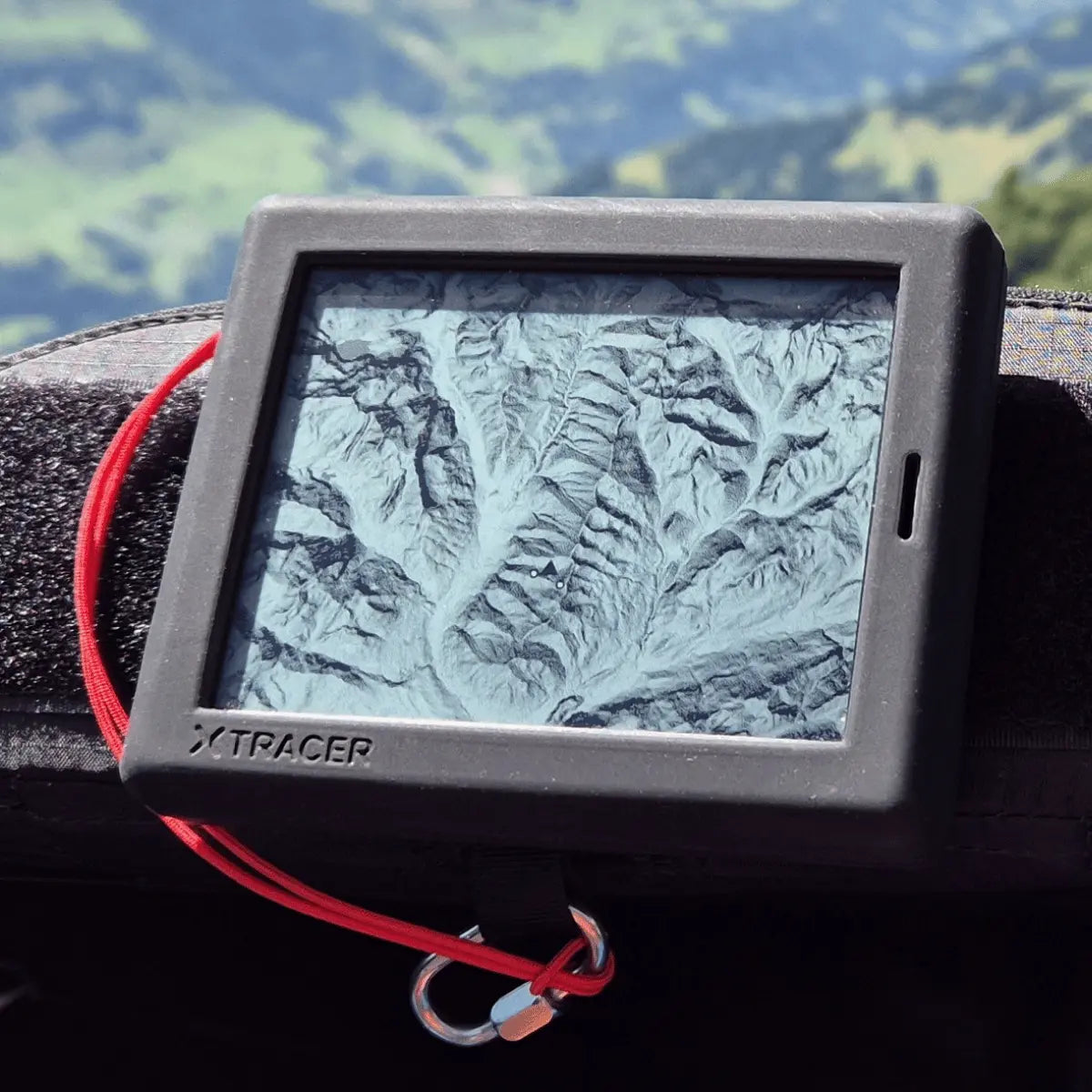 XC Tracer Maxx 3 Variometer in Silikonhülle mit rotem Lanyard, zeigt Terrainkarte auf E-Ink-Display, platziert auf Gleitschirmstoff.
