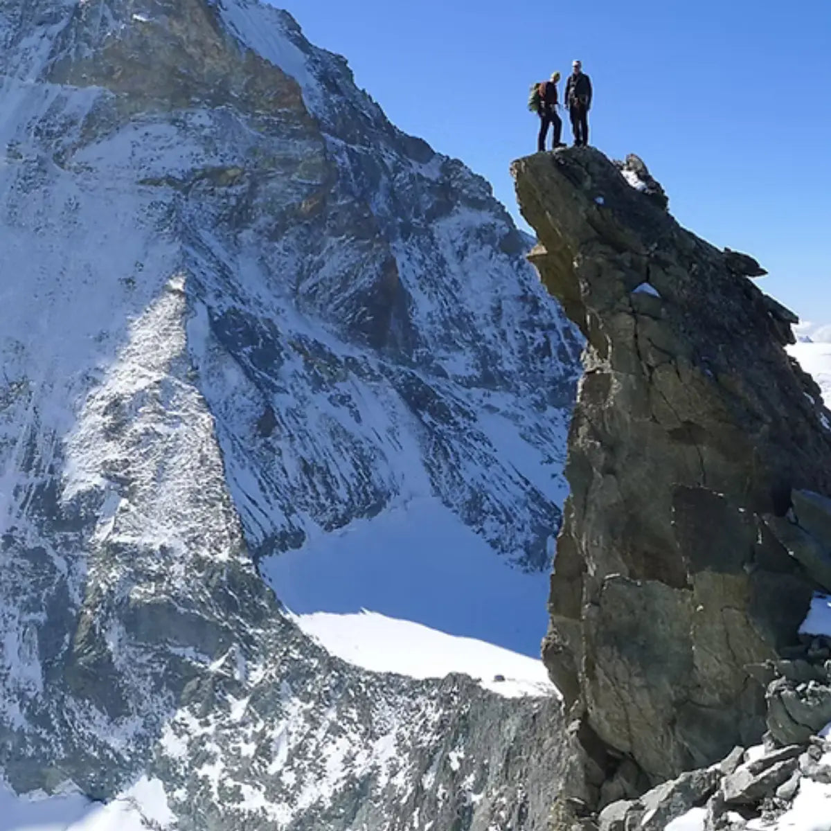 Zwei Bergsteiger auf einem Felsvorsprung mit verschneiten Bergen im Hintergrund, inspiriert von XPeaks - Neue Wege auf alte Berge!