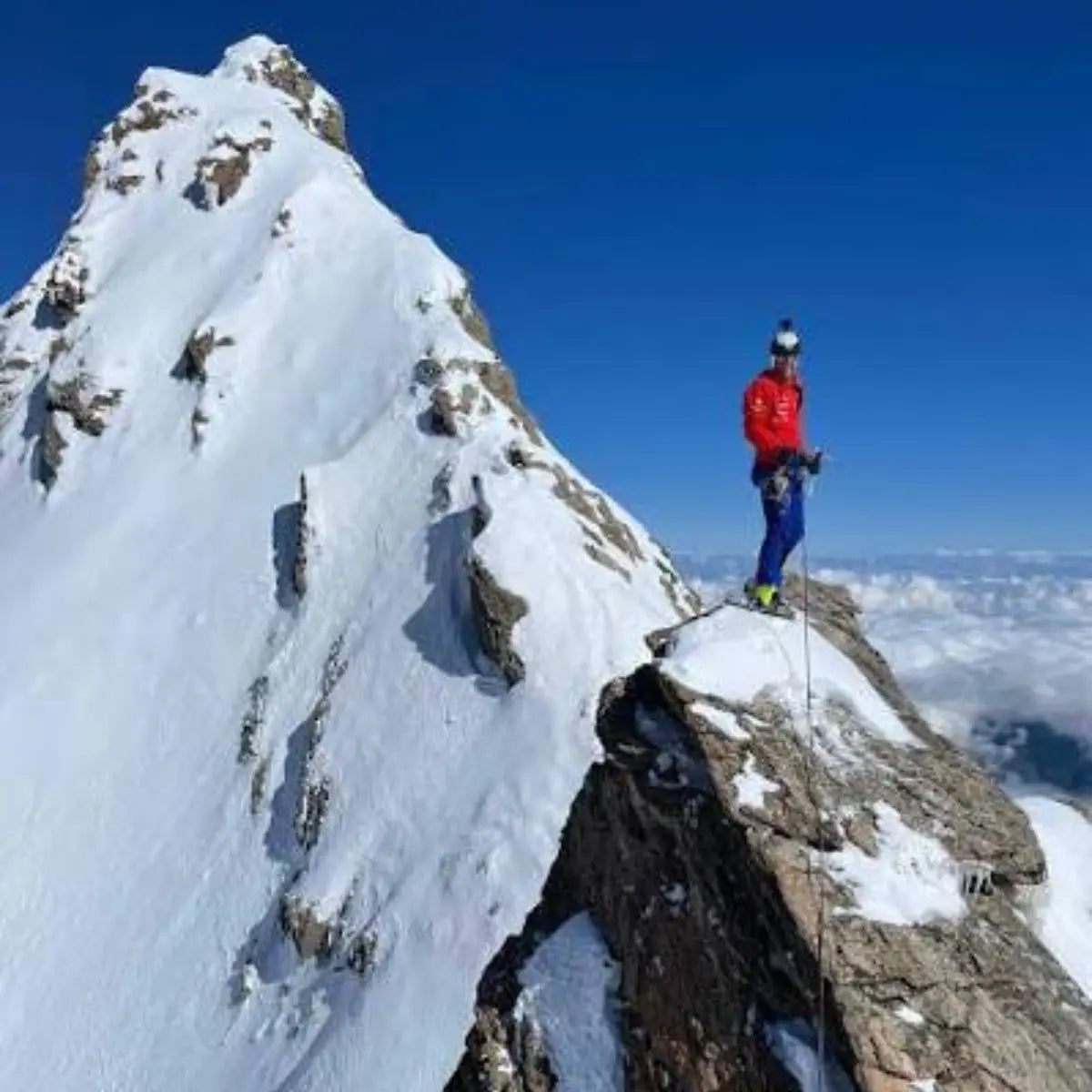 Ein Bergsteiger in roter Jacke und blauer Hose steht auf einem schneebedeckten Gipfel und blickt in die Ferne, mit dem Schriftzug "XPeaks - Neue Wege auf alte Berge!" im Hintergrund.