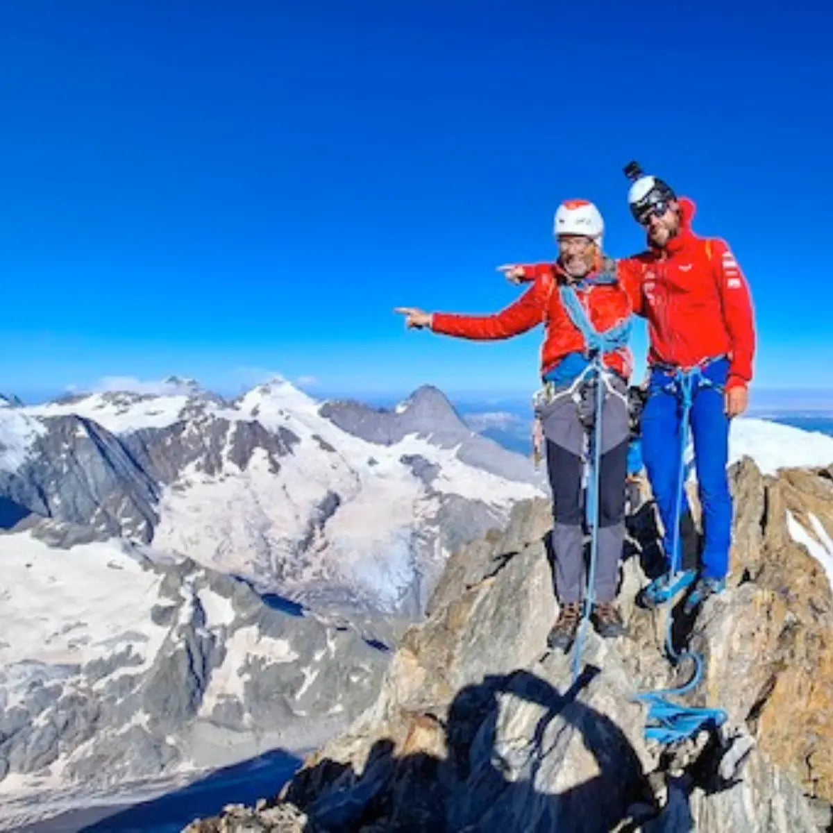 Zwei Bergsteiger in roter XPeaks-Bekleidung auf einem Gipfel mit Blick auf die Alpen.