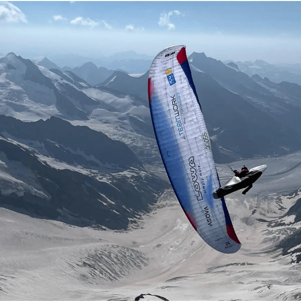 Paraglider mit LOWA-Branding fliegt über schneebedeckte Berge, inspiriert von "Neue Wege auf alte Berge!