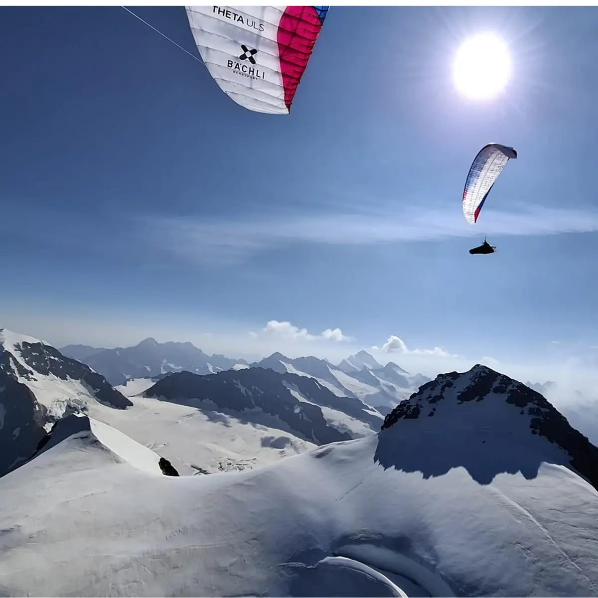 Zwei Gleitschirmflieger mit bunten Schirmen gleiten über schneebedeckte Berggipfel im Sonnenlicht, eine neue Perspektive auf Berge.