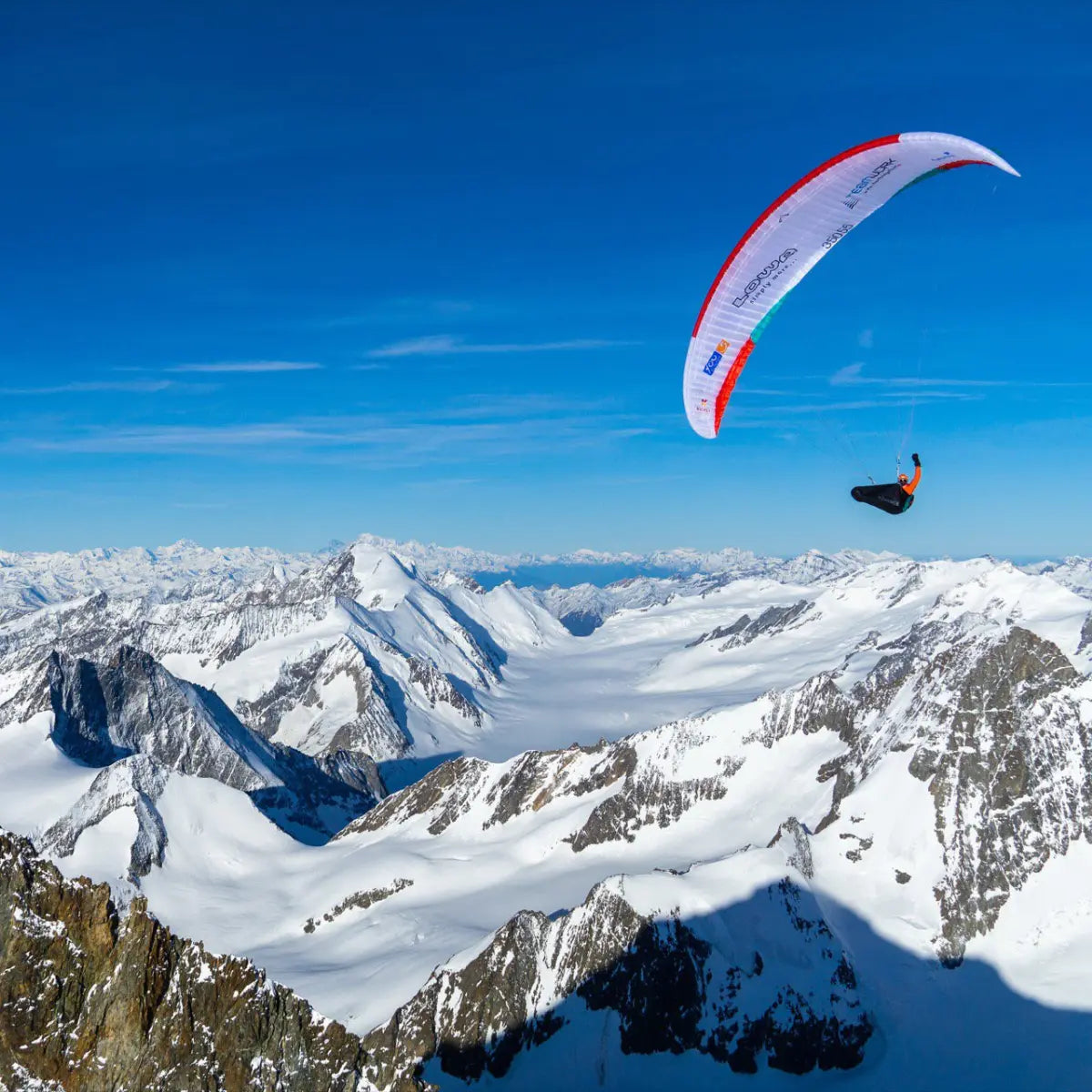 Paraglider mit roten und weißen Streifen fliegt über schneebedeckte Alpenlandschaft, inspiriert von XPeaks für neue Wege auf alten Bergen.