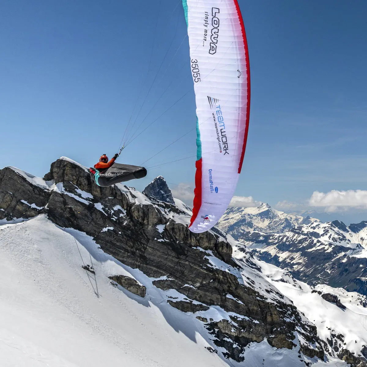 Ein Paraglider mit dem Aufdruck "LOWA" und "TEAMWORK" fliegt über schneebedeckte Berge, inspiriert von "Neue Wege auf alte Berge!".